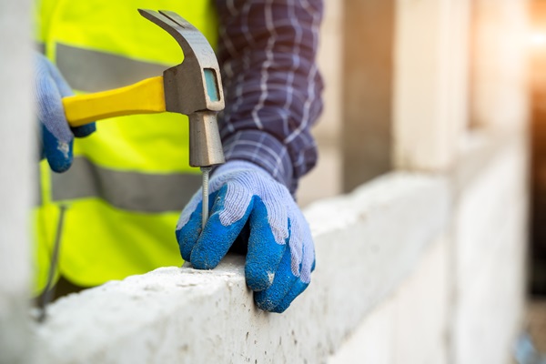 A construction worker wearing gloves and a safety vest hammers a nail into concrete while on a New York job site. (332871791)